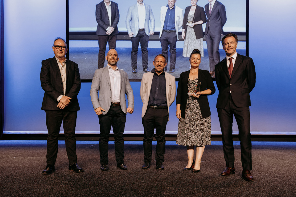 Five people stand on stage, one woman holds an award